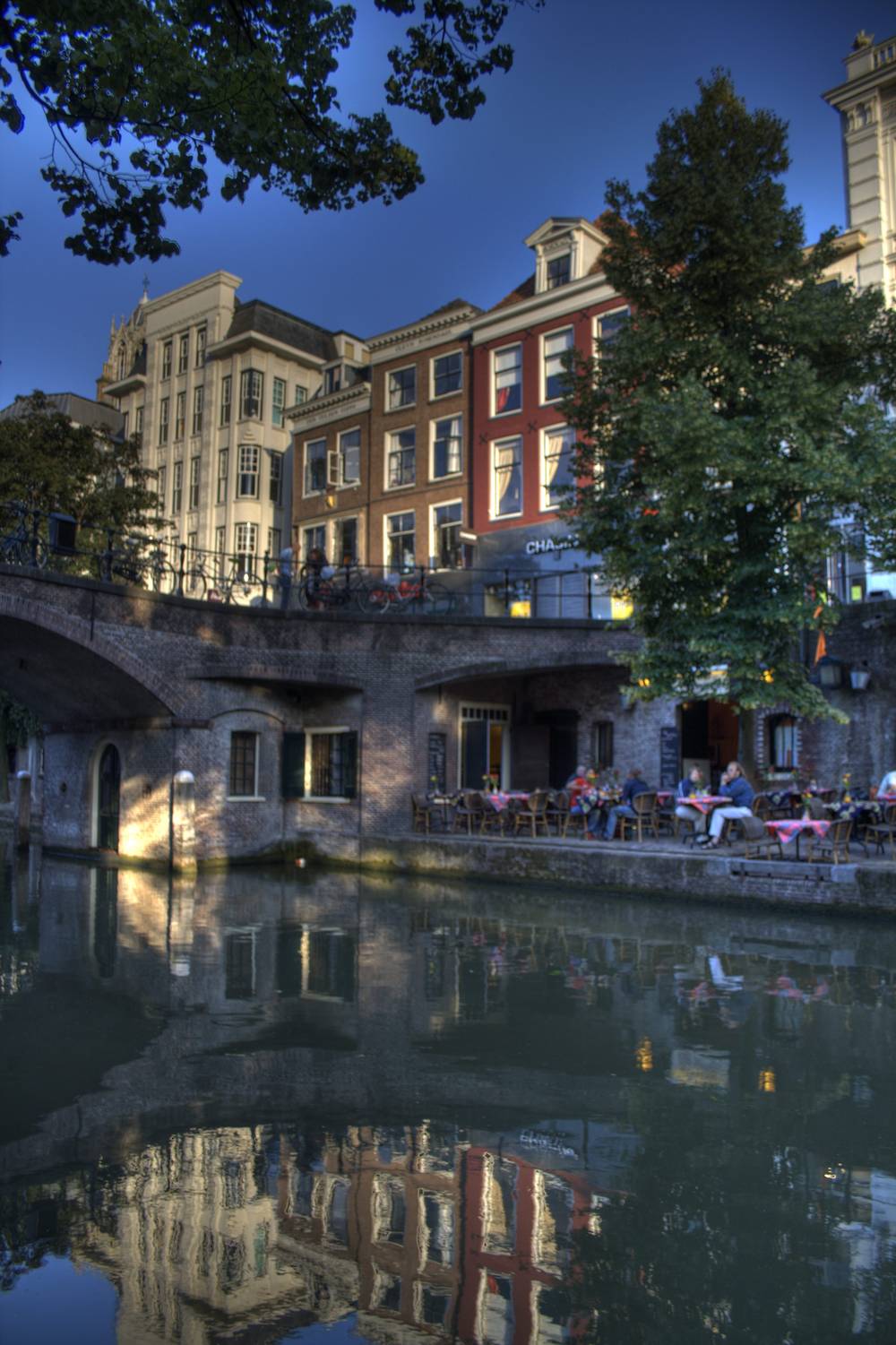 Historic canal-side buildings and an outdoor cafe reflected in the Oudegracht canal at dusk.