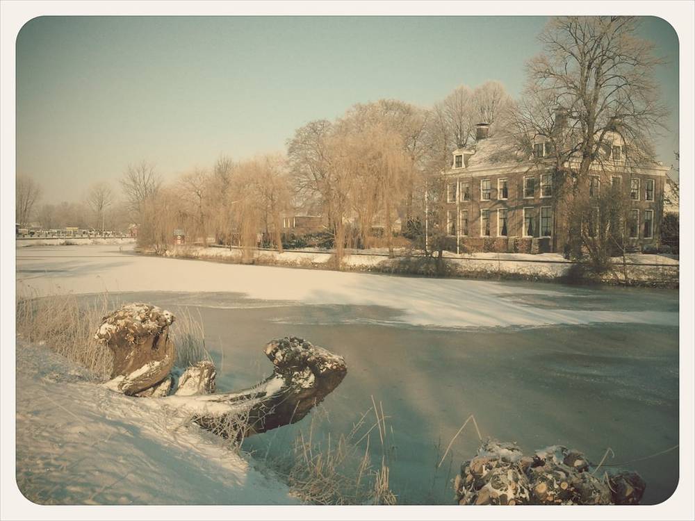 A frozen river winds past a grand old house dusted with snow.