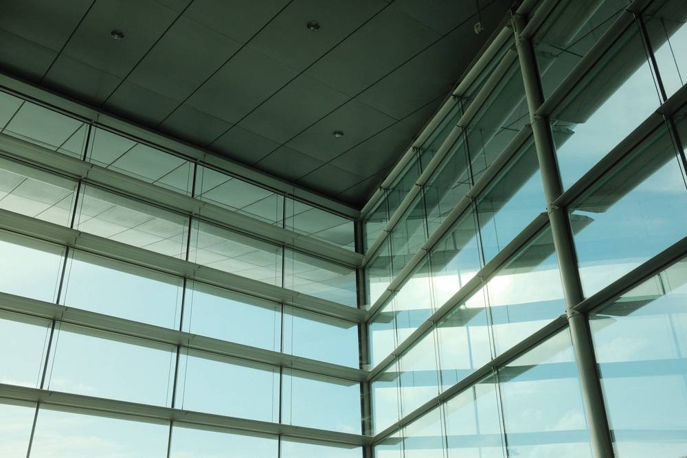 Upward view of intersecting glass curtain walls and ceiling at an airport terminal.