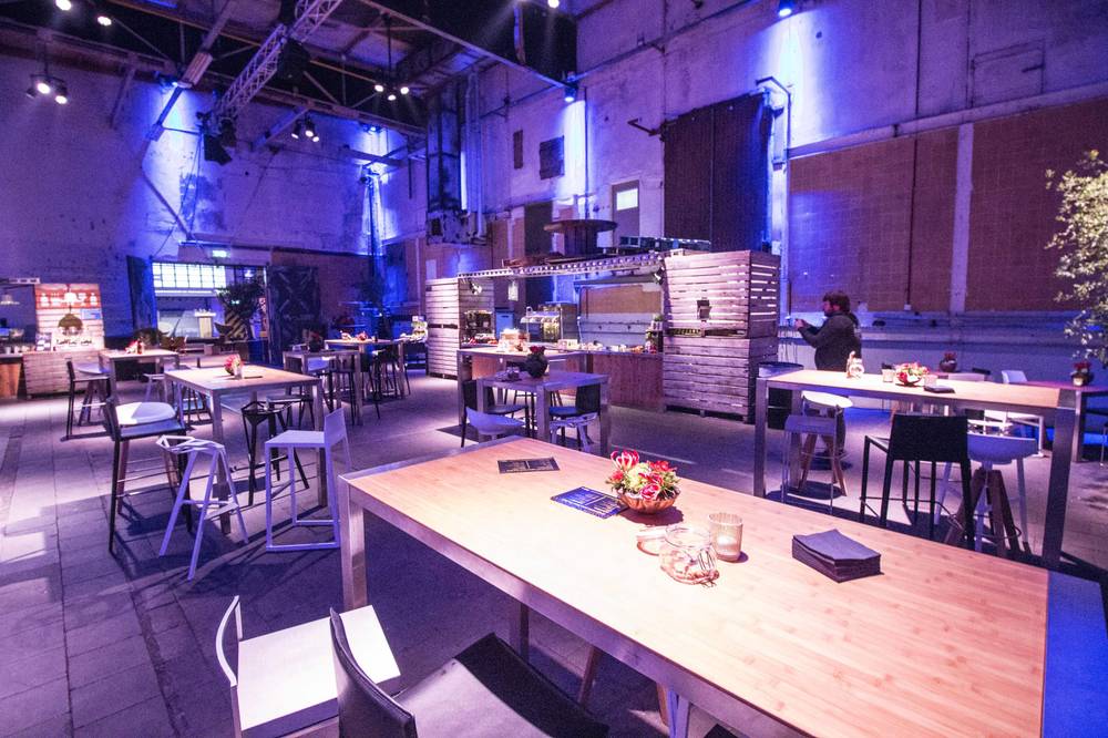 Empty tables are set with flowers ready for guests in the blue-lit hall at De Fabrique.