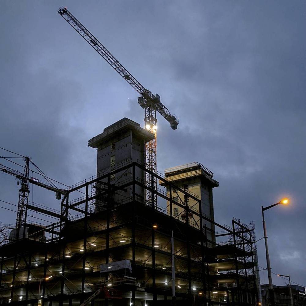 A building under construction with a crane, lit up at night.