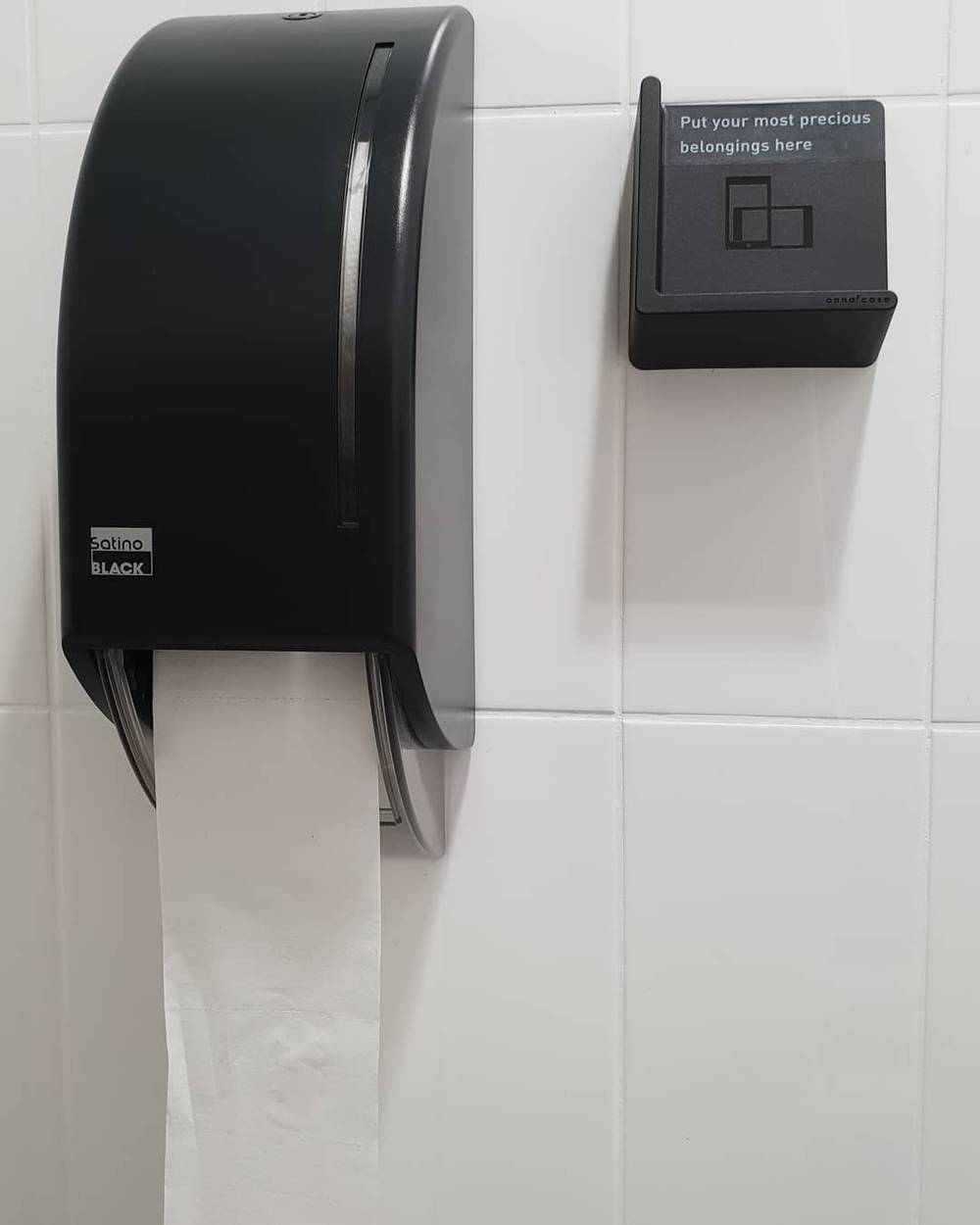 A toilet paper dispenser next to a small sign reading 'Put your most precious belongings here'.