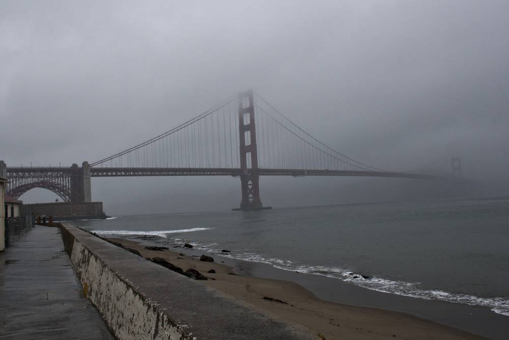 The Golden Gate Bridge fades into fog above a curving seawall path.