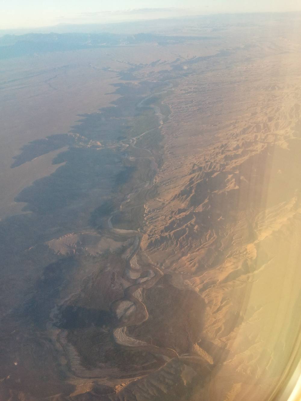 Aerial view of dry canyon terrain seen through a plane window at sunset.