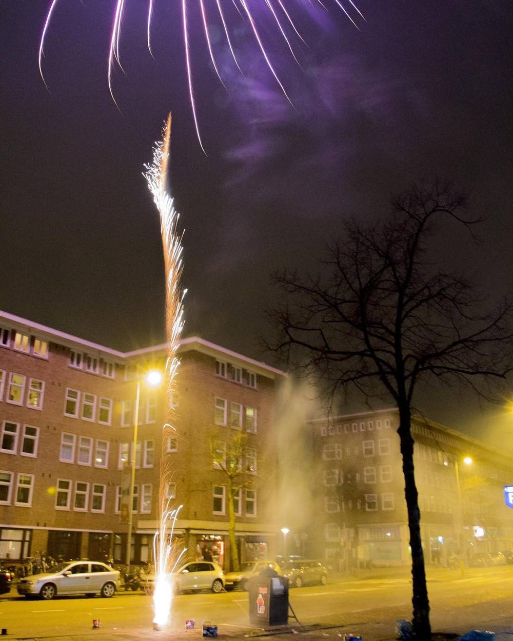 A firework rocket bursting in the sky above rooftops at night.