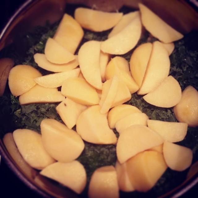 Sliced potatoes arranged on top of dark greens in a cooking pot.