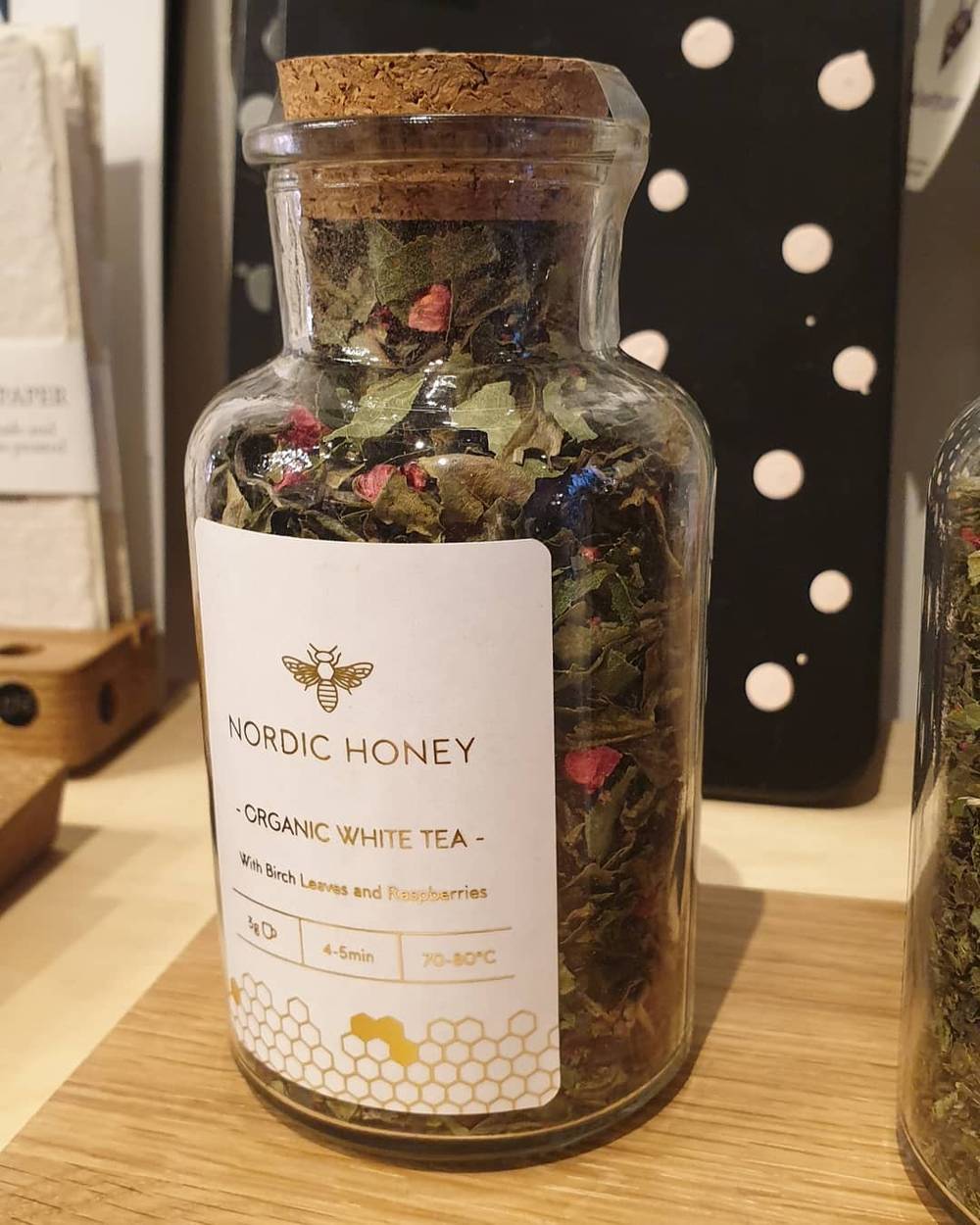 A glass jar labeled "Nordic Honey, Organic White Tea" is filled with dried herbs and berries.