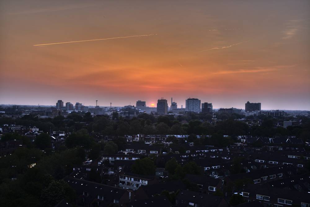 The sky glows deep orange at sunset over the Utrecht skyline and rooftops.