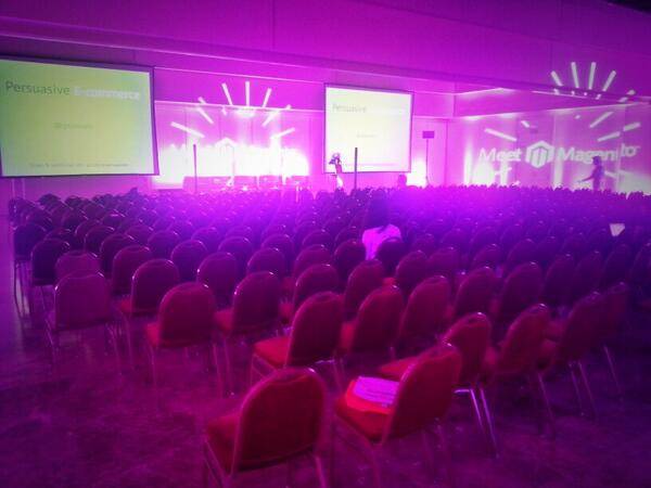 A large seated audience in a purple-lit conference hall before a presentation.