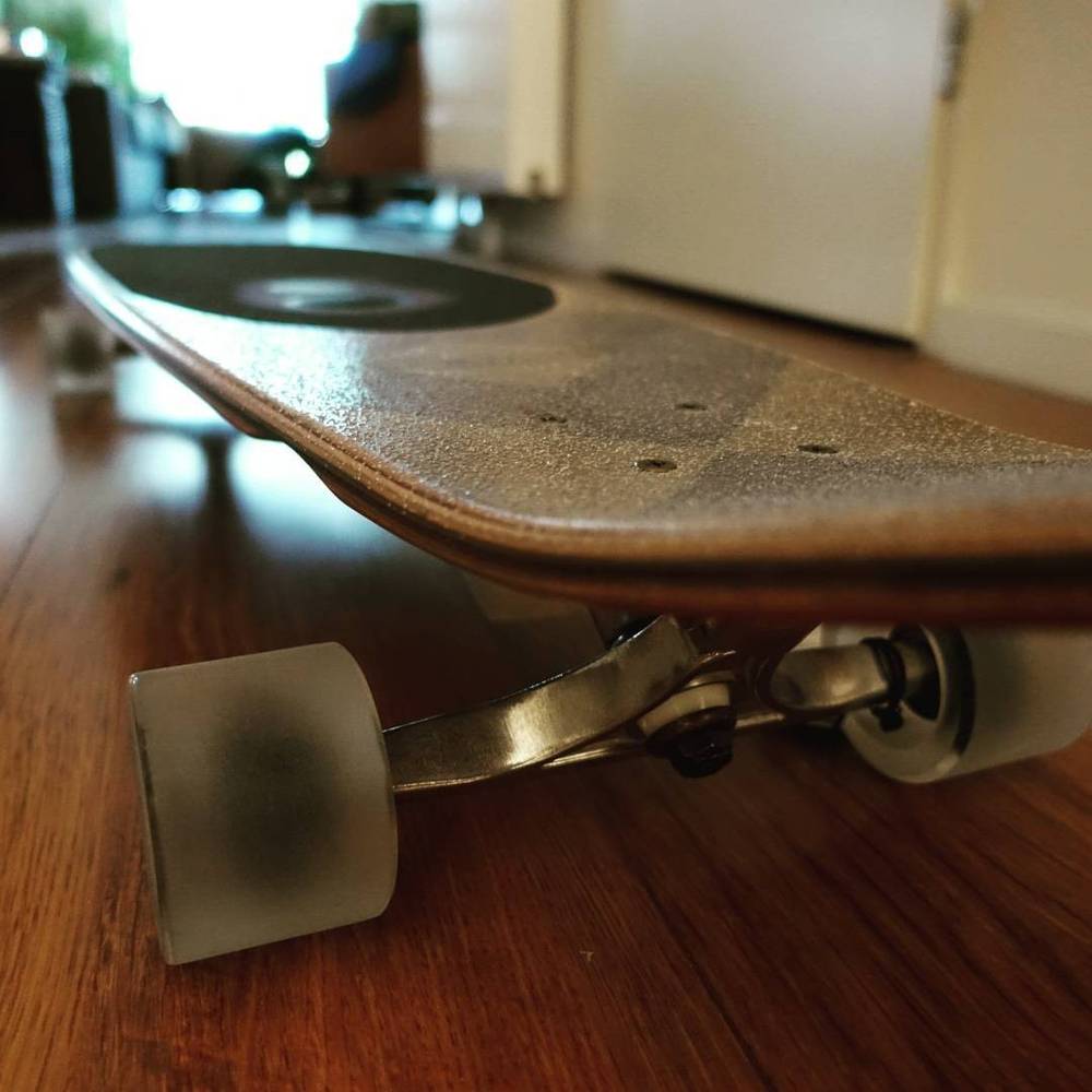 Close-up of a skateboard's underside and wheel on a wooden floor.