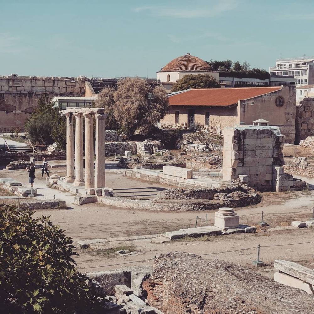 Ancient temple ruins with standing columns, next to a domed Byzantine church in Athens.