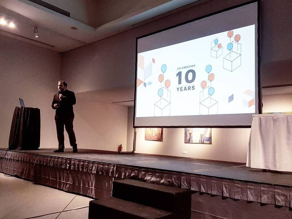 A man presenting on stage in front of a slide reading "Celebrating 10 Years," at the Meet Magento Greece conference.