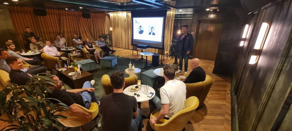 A small group seated in lounge chairs watching a presentation in a dimly lit venue.