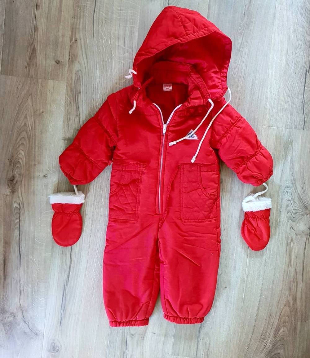 A red hooded baby snowsuit with mittens laid out on a wooden floor.