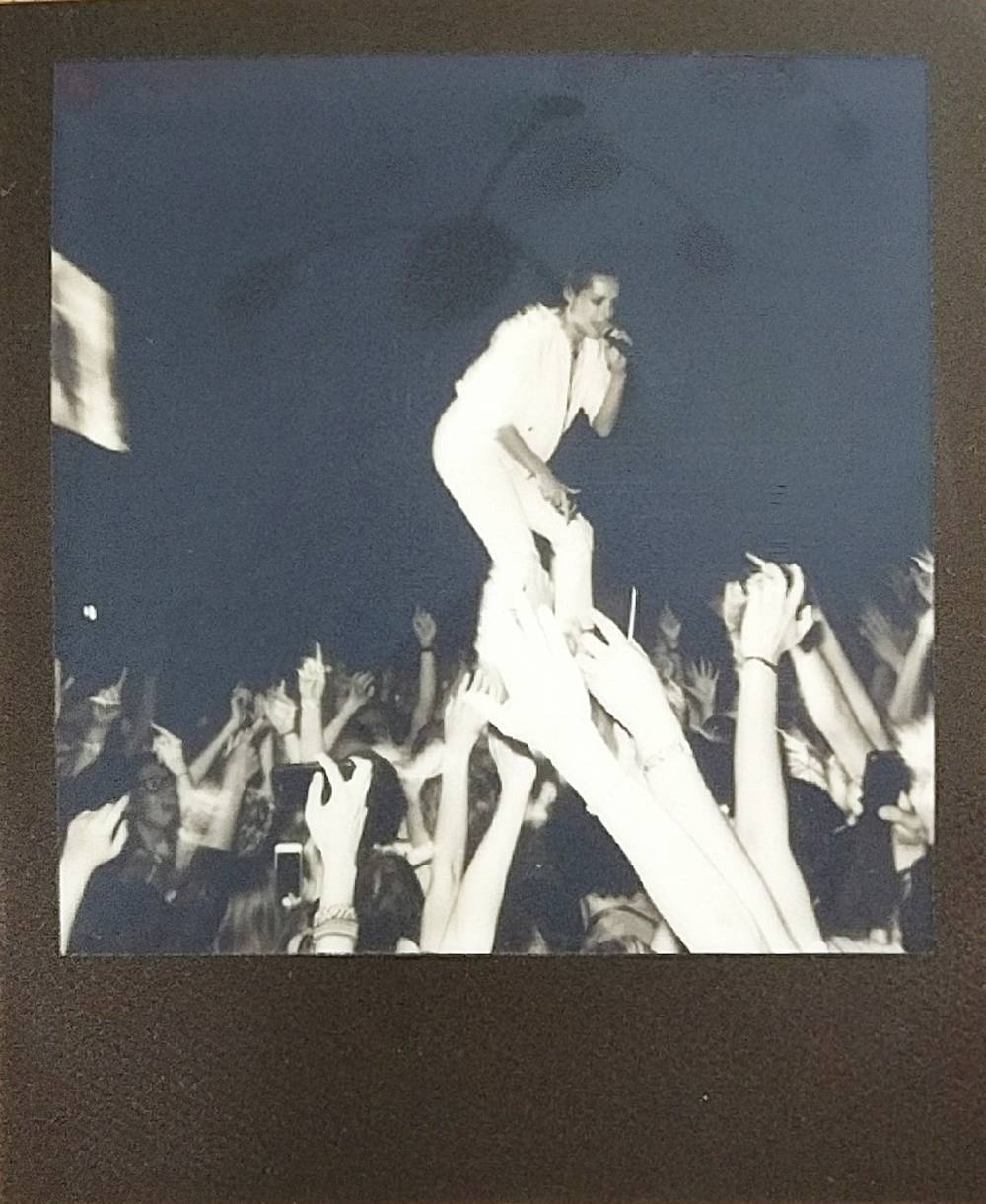 Black and White flash polaroid of Kali Uchis walking into the audience on the hands of the crowd singing