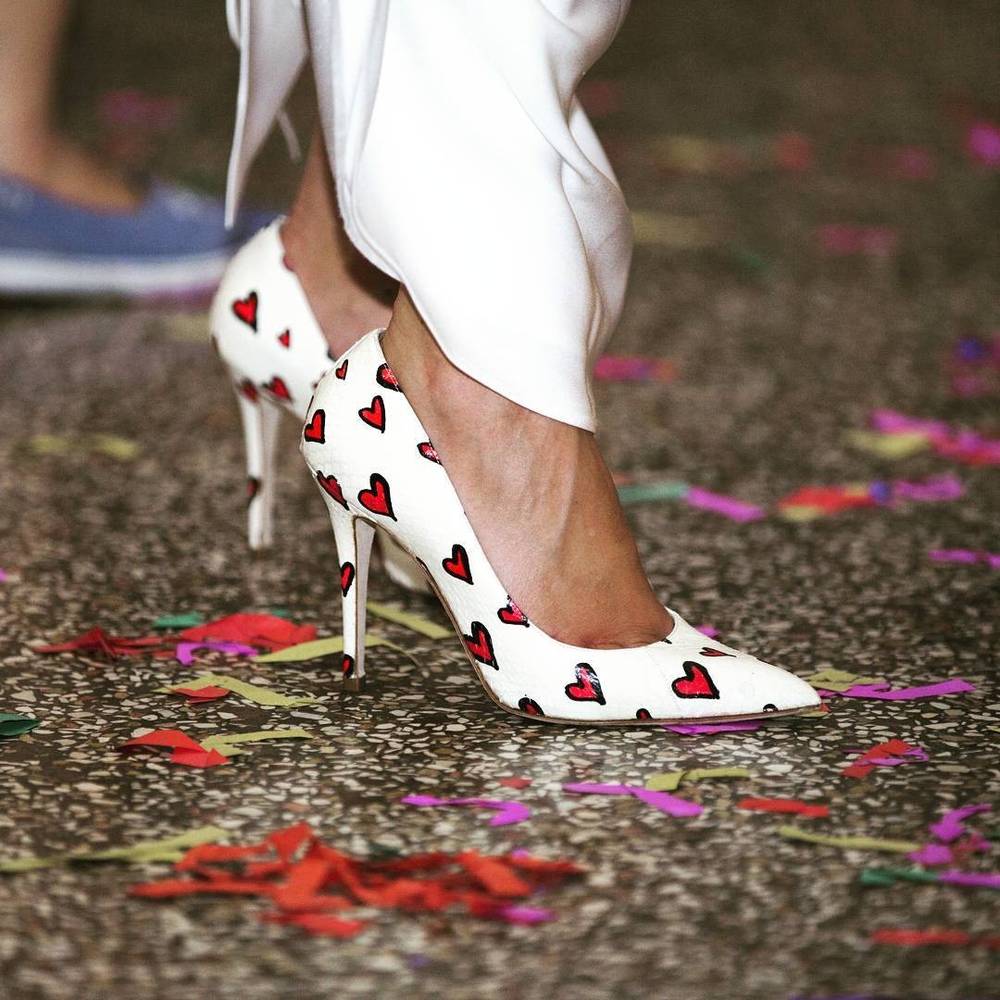 White high heels printed with hearts standing on confetti-covered ground.