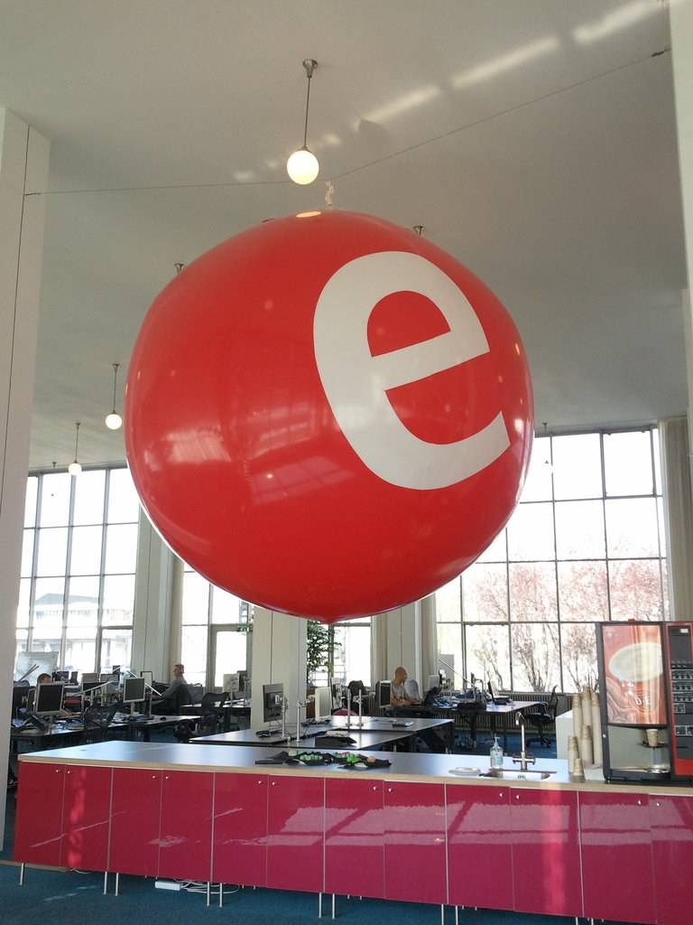 A giant inflatable red ball with a white 'e' logo hangs above an office space.