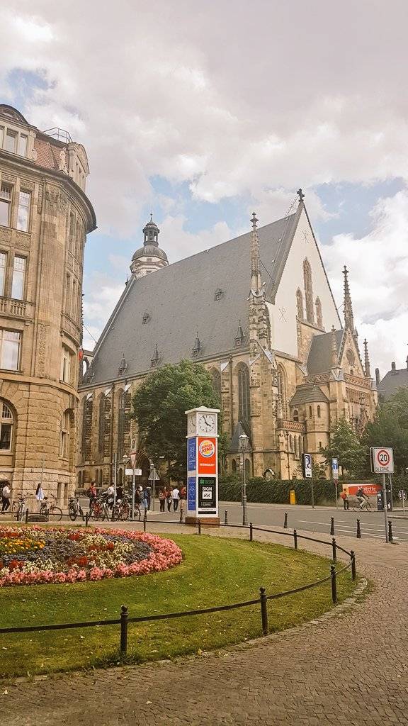 The spired facade of the Thomaskirche church in Leipzig, with flower beds in front.