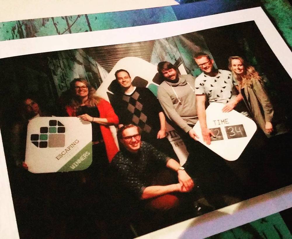 Group photo of five friends posing with an escape room "winners" sign and completion time.