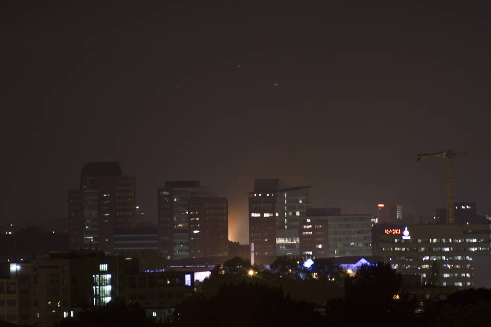 A distant orange glow of a factory fire lighting up the night sky above the city skyline.