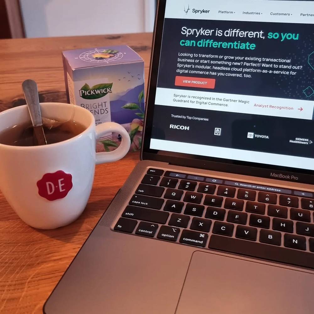 A laptop displaying the Spryker company website next to a cup of coffee on a wooden table.