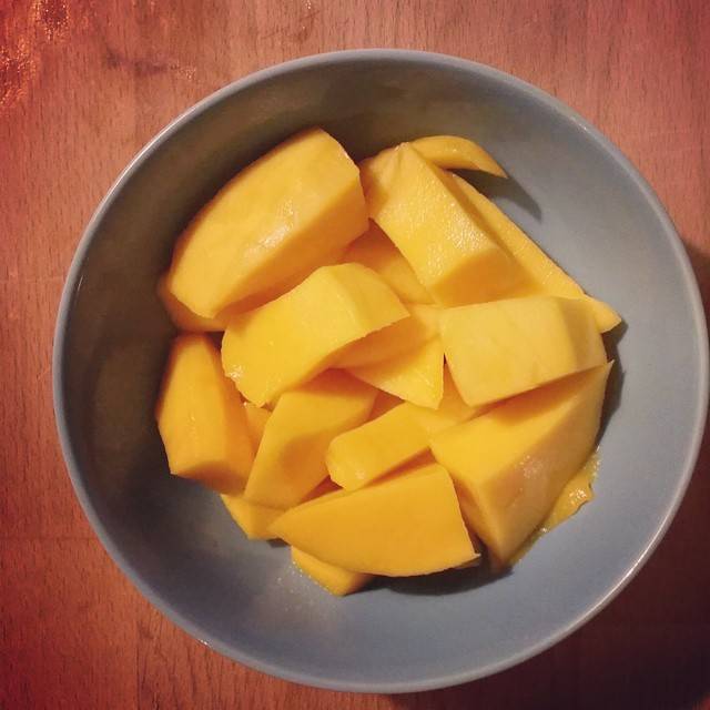 A bowl of cut mango pieces on a wooden table.