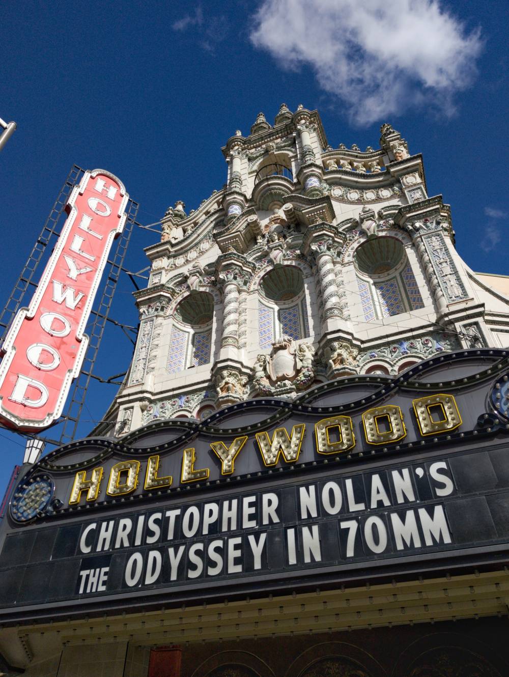The marquee of the Hollywood Theatre in Portland, OR - a 100 year old theater with an intricate facade. The marquee says "CHRISTOPHER NOLAN'S THE ODYSSEY IN 70MM"