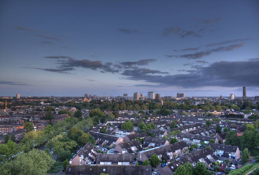 A pale dawn sky with scattered clouds glows over the Utrecht skyline and rooftops.