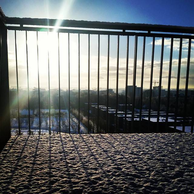 Sunlight streaming through a railing onto a frosty balcony overlooking a city.