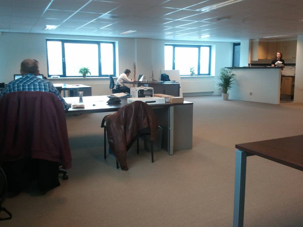 Colleagues work at desks in a bright, half-furnished open office.