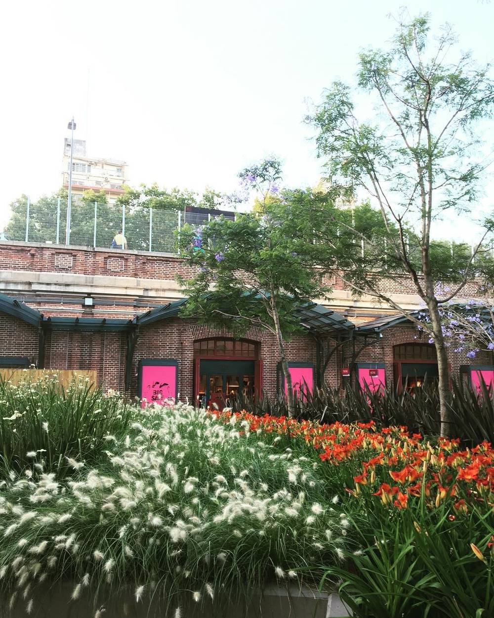 A garden with red and white flowering plants in front of a red brick market building.