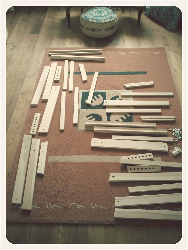 Unassembled flat-pack furniture pieces are laid out in order on a rug.