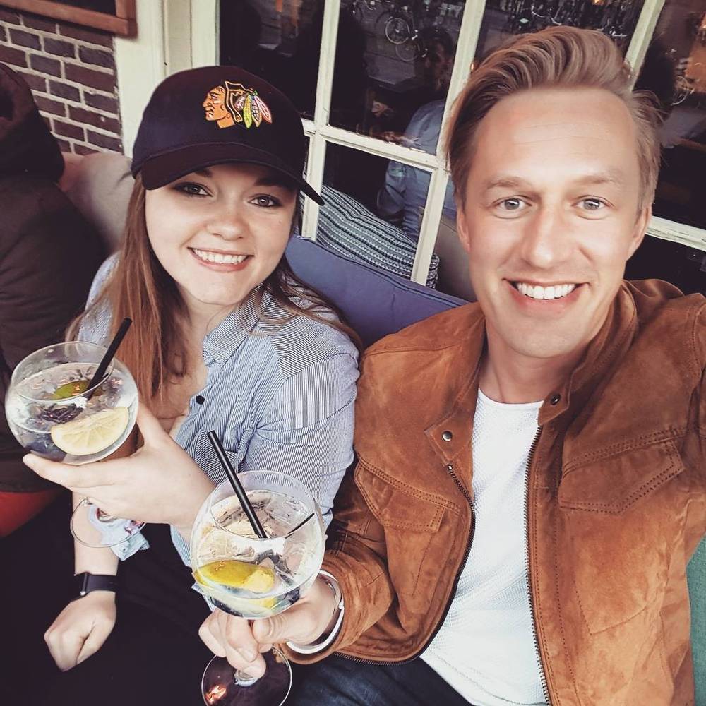 A man and woman pose with cocktails for a selfie in a bar.