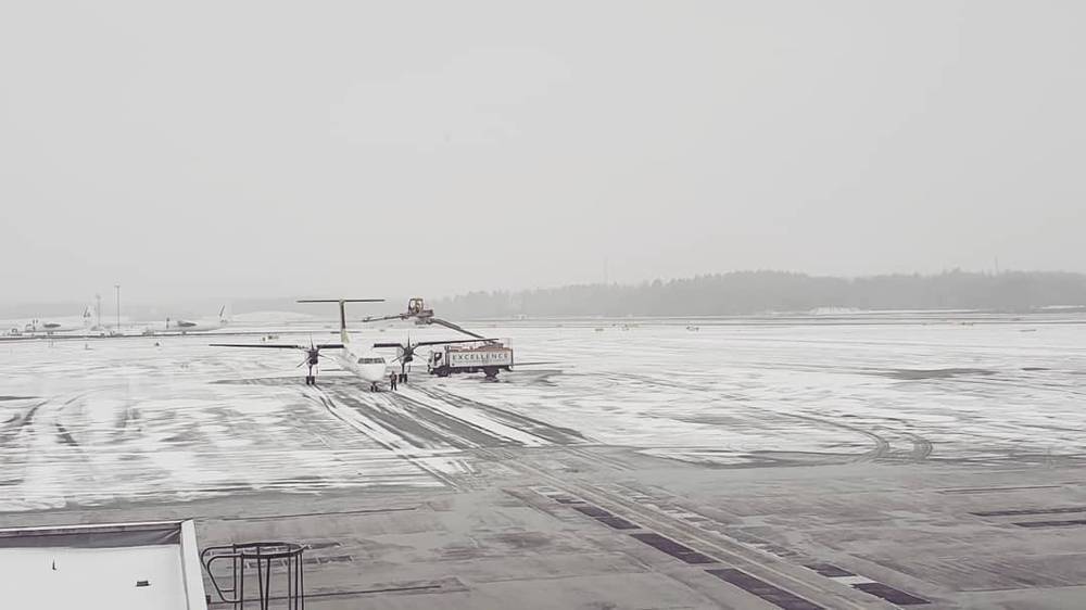 A small propeller plane sits on a snowy, foggy airport tarmac.