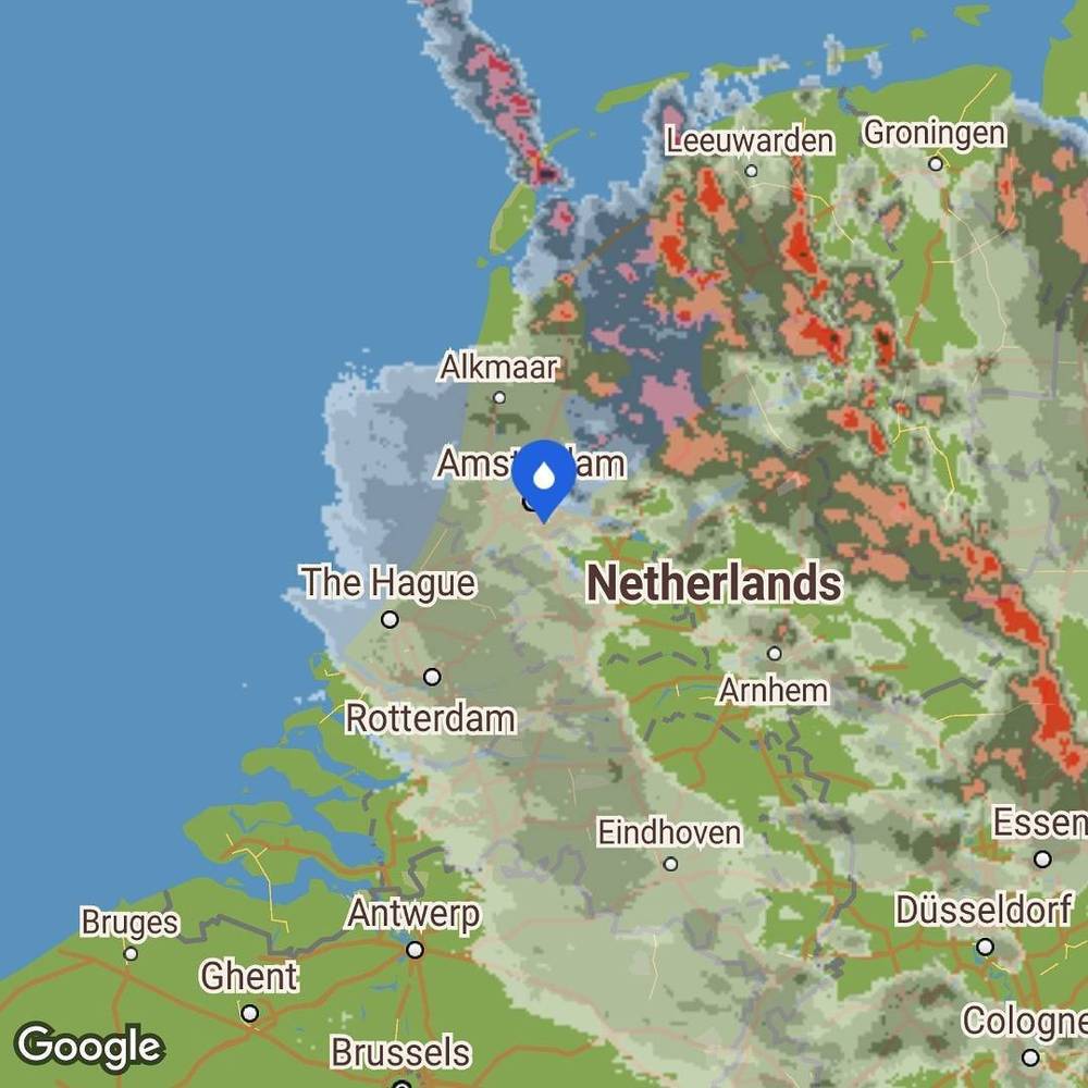 A weather radar map of the Netherlands showing rain clouds over Amsterdam and the west coast.