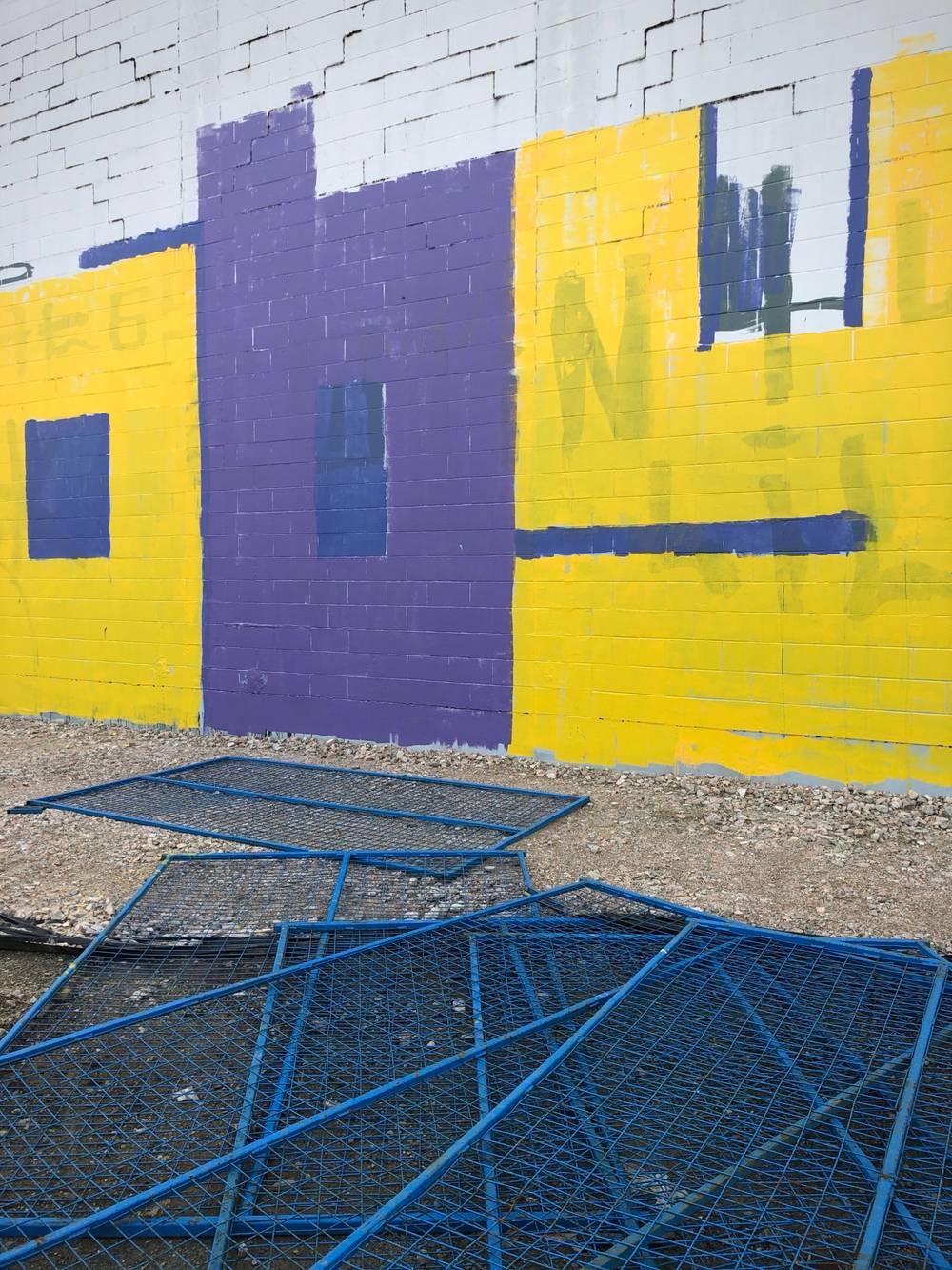 Purple and yellow graffiti on a wall with blue fencing scattered in the foreground