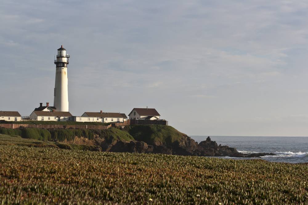 A white lighthouse and cluster of keeper's houses stand on a coastal bluff.