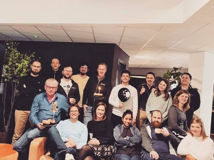 A team poses together celebrating in an office lounge with party hats and treats.