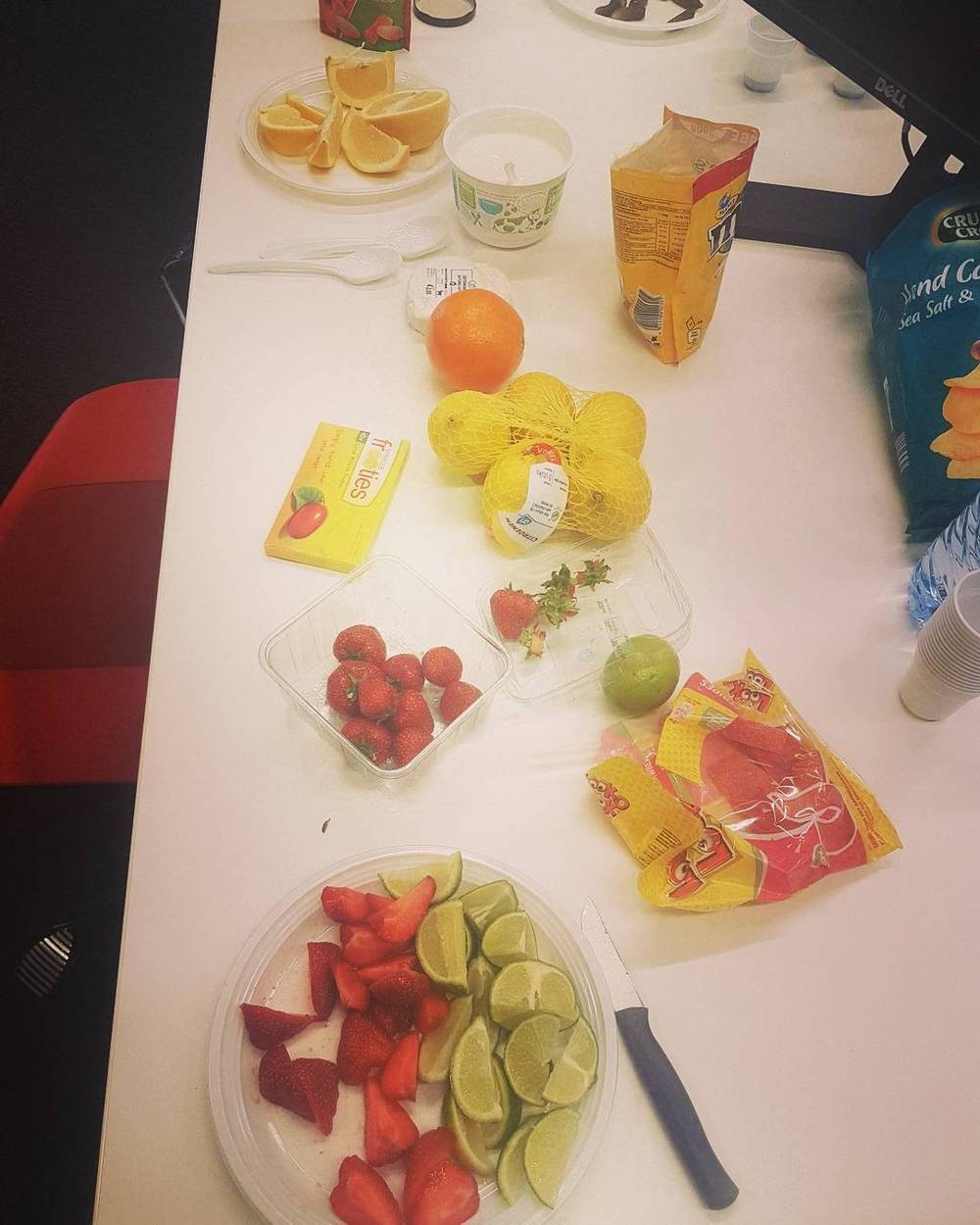 A breakfast table with sliced fruit, strawberries, limes, and packaged snacks.