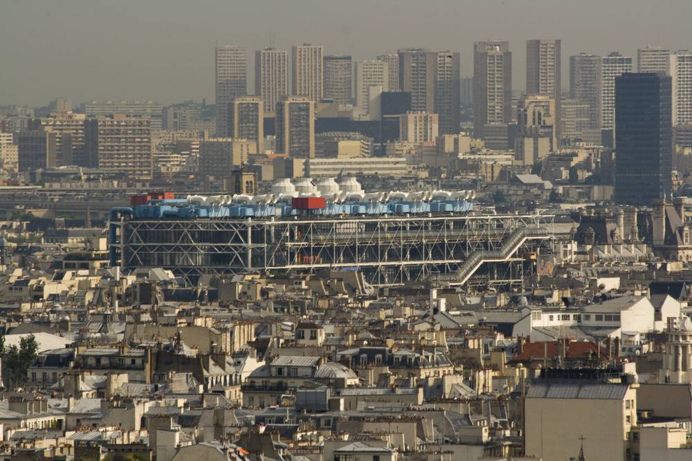 The Centre Pompidou's colorful pipework stands out among Paris rooftops under a hazy sky.