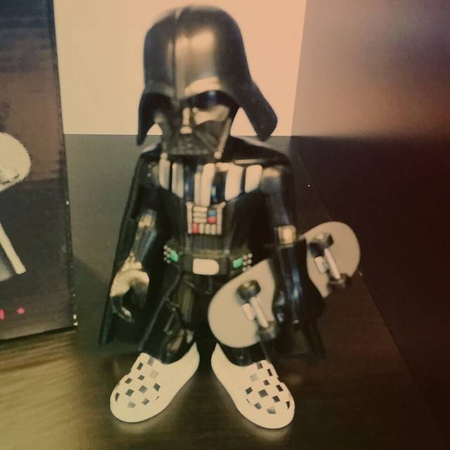 A Darth Vader action figure with skateboard-style feet standing on a table.