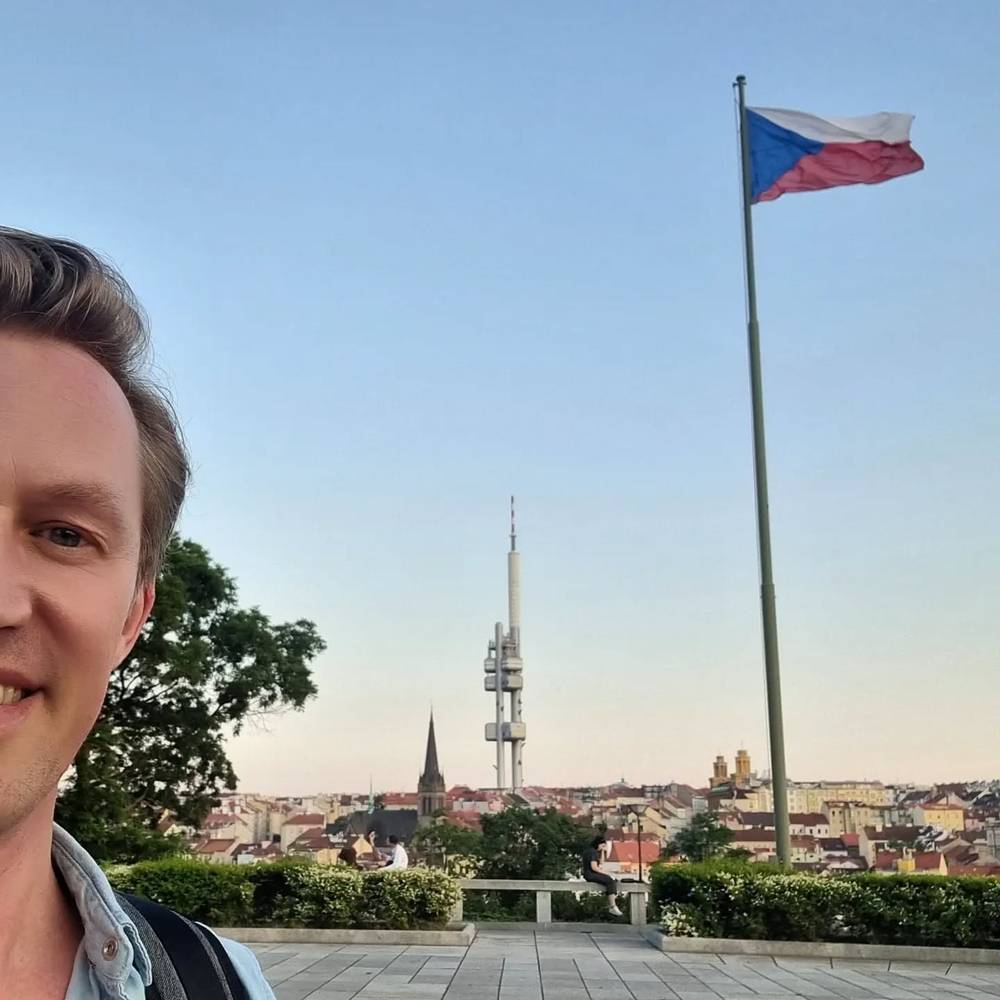 Guido in a selfie with the Czech flag and Prague's television tower visible over the city skyline.