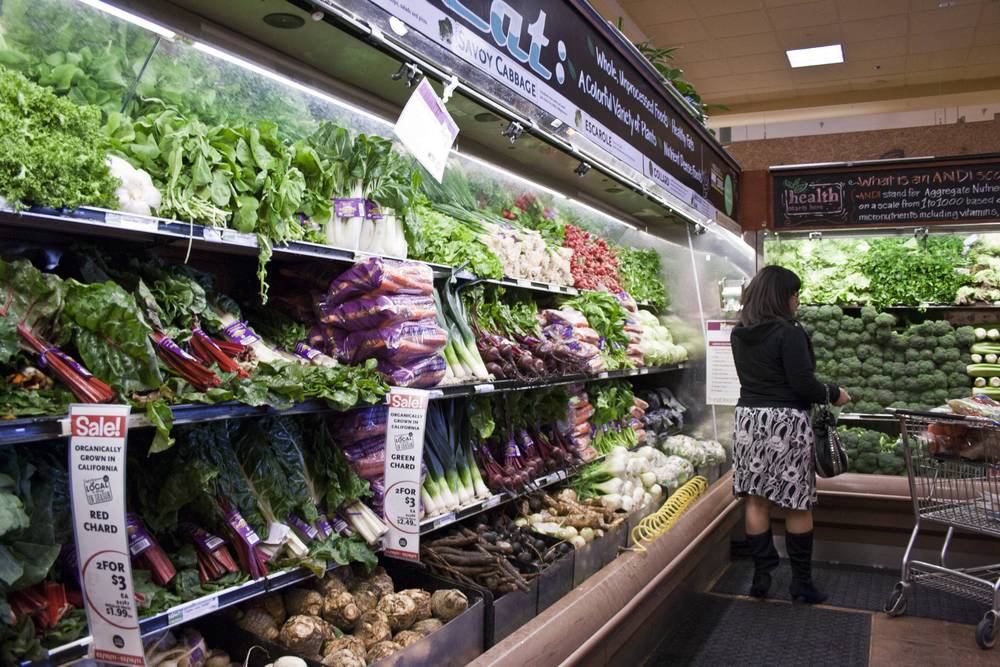 A shopper browses a well-stocked produce aisle of leafy greens at a grocery store.