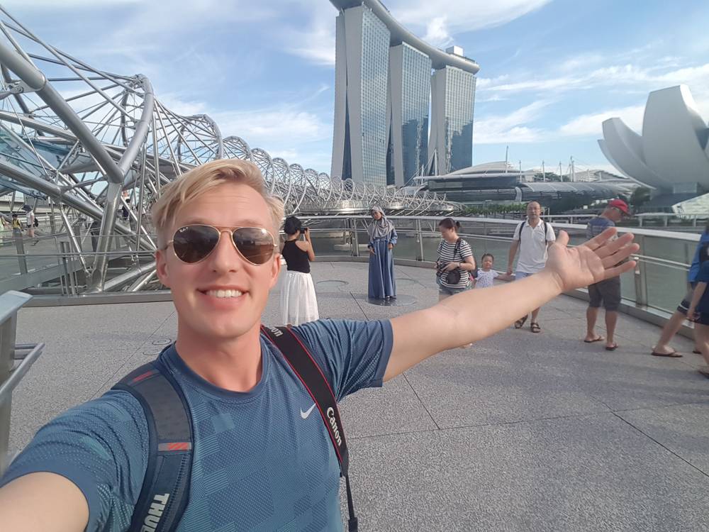Guido takes a selfie on a bridge, with Marina Bay Sands and the ArtScience Museum behind him.