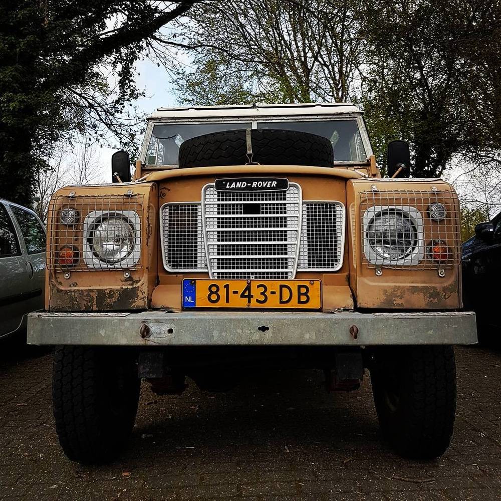 A vintage orange Land Rover Series 3 parked among trees.