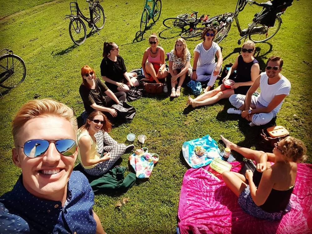 Overhead selfie of a group of friends sitting on a picnic blanket with bicycles nearby.