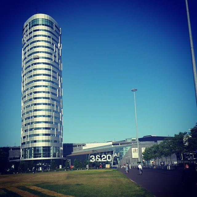 A tall modern glass office tower against a clear blue sky, with a building reading '3&20A' nearby.