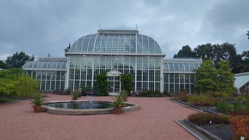 A glass greenhouse building with a fountain in a formal garden.