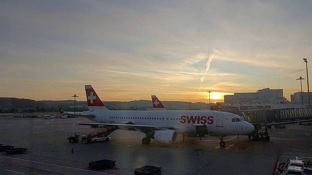 Two Swiss International Air Lines planes parked at the gate during a colorful sunset.