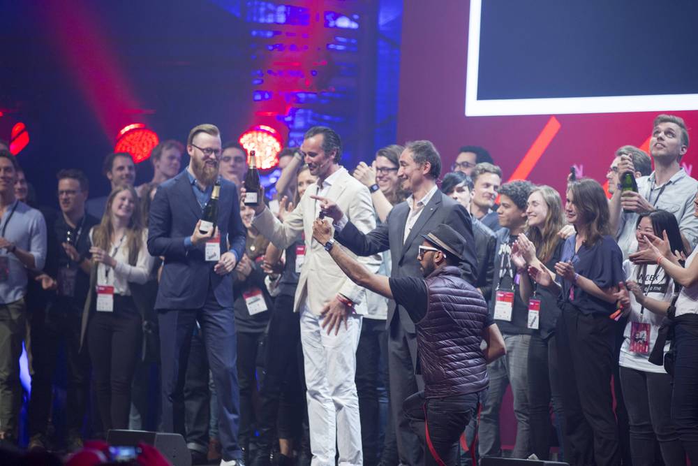 A group on stage cheers and shakes hands together with a champagne bottle in hand.